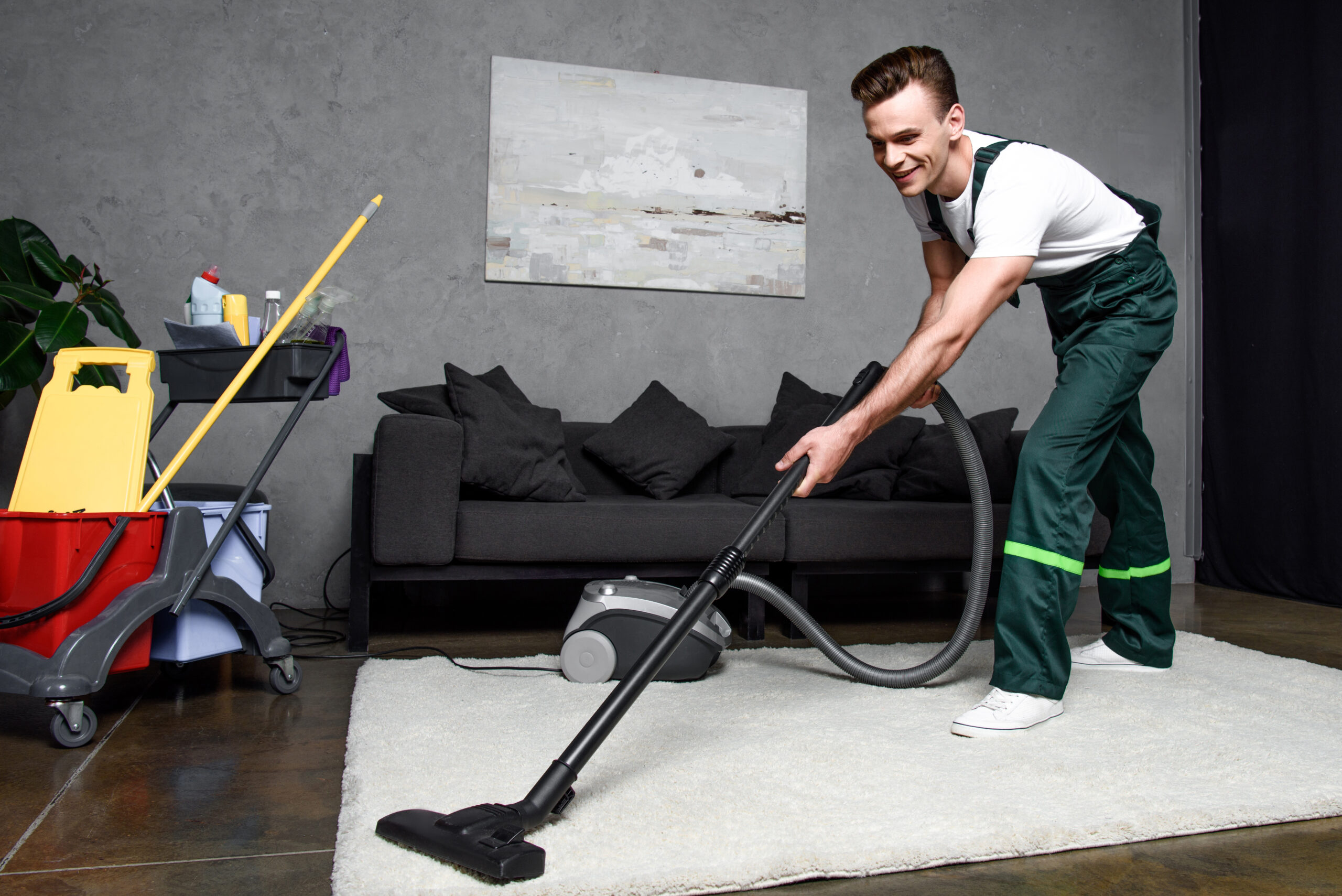 smiling young professional cleaner cleaning carpet with vacuum cleaner