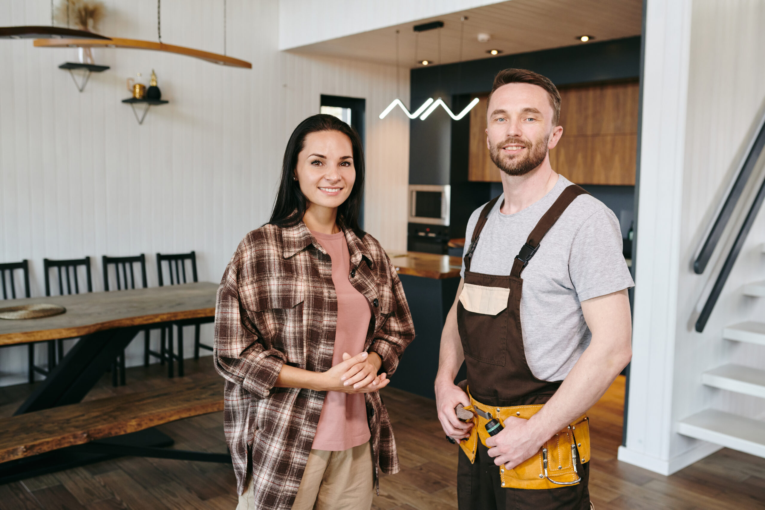 Young woman and plumber looking at you while standing in living-room